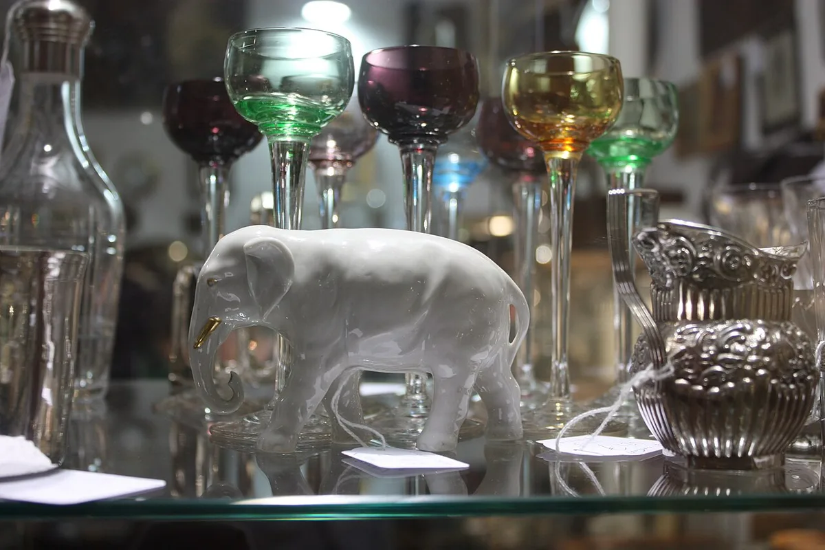Weiße Porzellanfigur eines Elefanten zwischen bunten Kristallgläsern in einer Vitrine